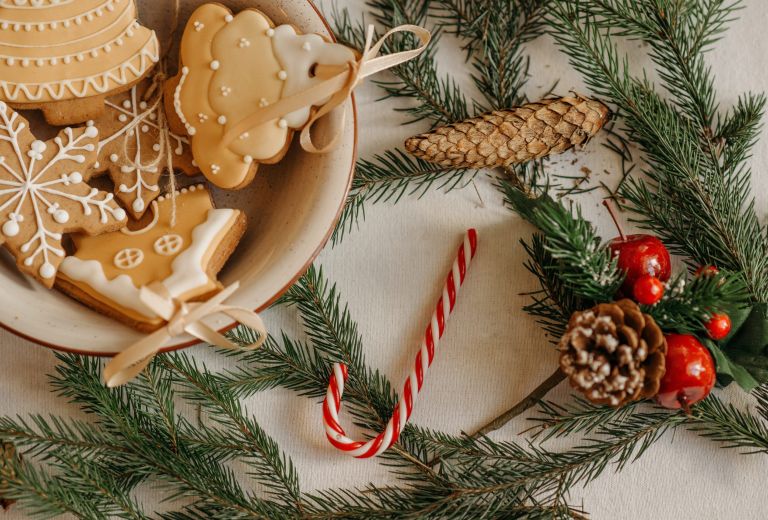Foto van kerstkoekjes, dennentakken en een zuurstok.